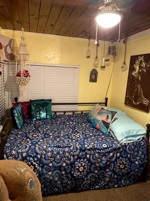A bedroom with a patterned bedspread, a hanging light fixture, and a wall-mounted picture. - Whimsical Mermaid Retreat with Private Deck in Bacliff, Texas (Bacliff)