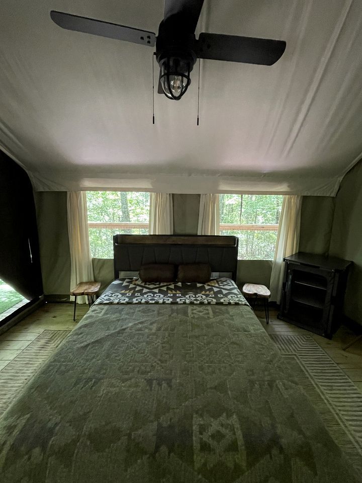 A bedroom with a large bed, a ceiling fan, a small table, and a fireplace.
