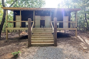 A wooden cabin with a staircase leading to a door, surrounded by trees.