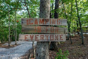 A wooden signpost with the message 'Camping is for everyone' in a wooded area.