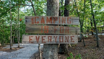 A wooden signpost with the message 'Camping is for everyone' in a wooded area.