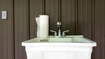 A white pedestal sink with two faucets, a paper towel holder, and a visible pipe beneath.