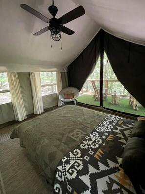 A tent-style room with a ceiling fan, a bed with patterned bedding, a chair, and a view of the outdoors. - Mountain Glamping Tent with Sunrise Views & Firepit in Rising Fawn, Georgia (Rising Fawn)