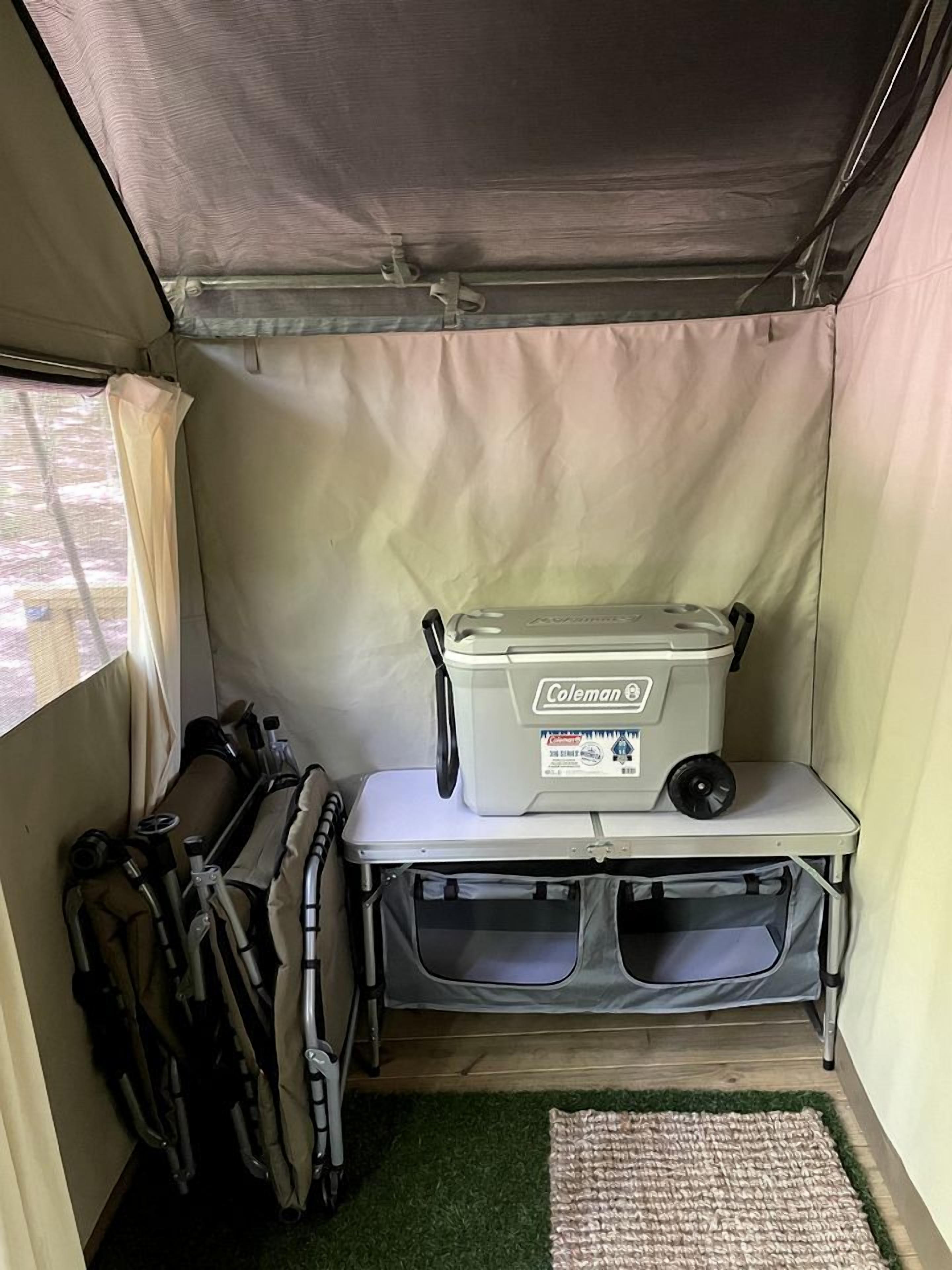 Un intérieur de tente compact comprenant une glacière Coleman, une petite table et du matériel de camping.