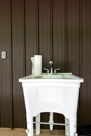 A white pedestal sink with two faucets, a paper towel holder, and a visible pipe beneath.