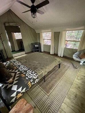 Une chambre avec un grand lit, un ventilateur de plafond, une fenêtre avec des rideaux et une petite table.