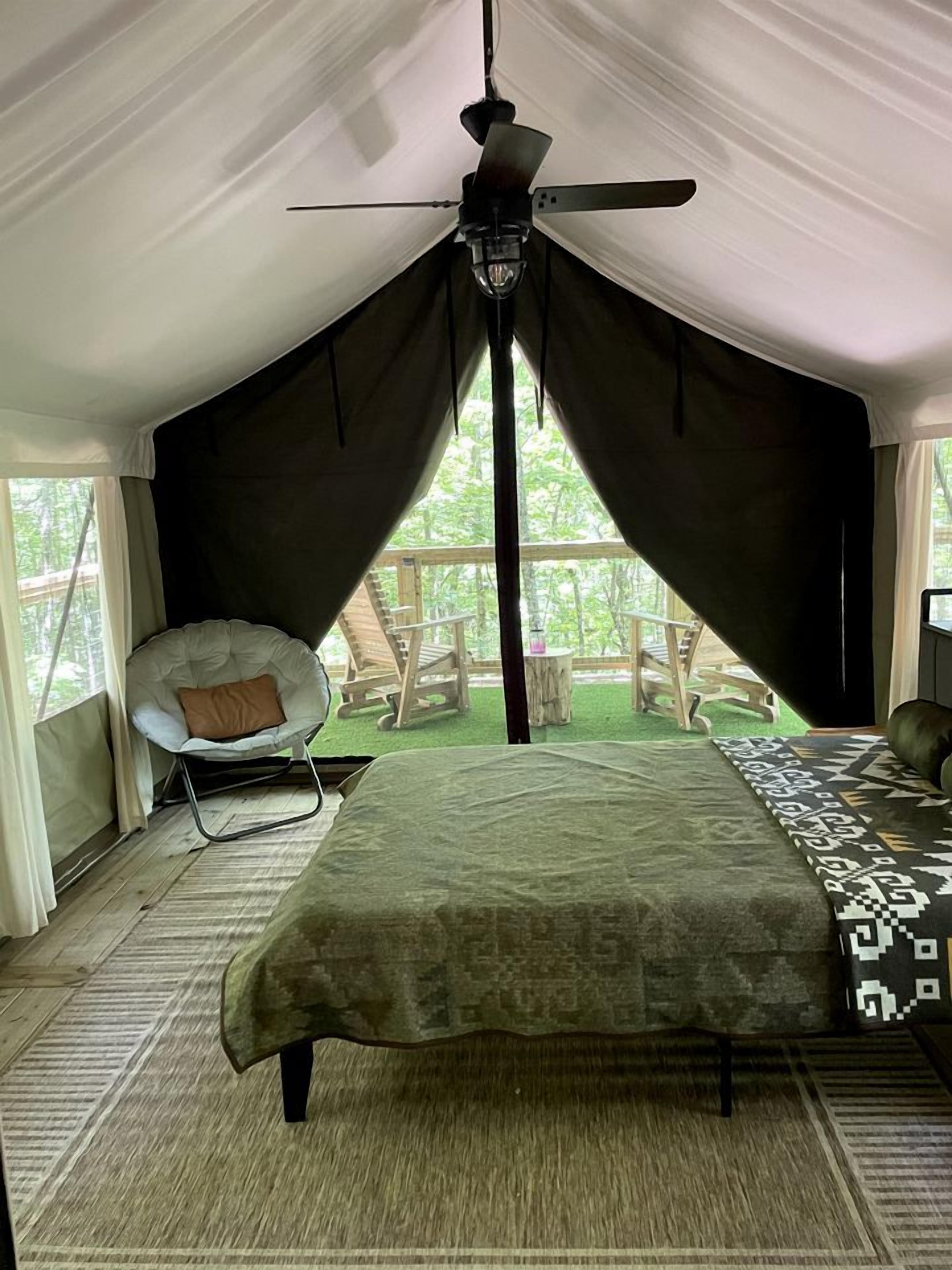 A tented room with a bed, a chair, and a ceiling fan.