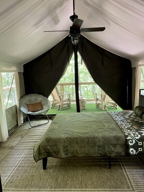 Une pièce aménagée avec une tente, un lit, une chaise et un ventilateur de plafond.