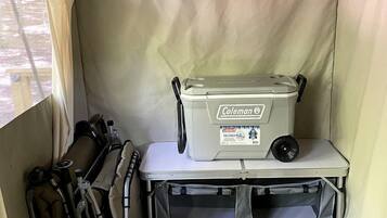 A compact tent interior with a Coleman cooler, a small table, and camping gear.