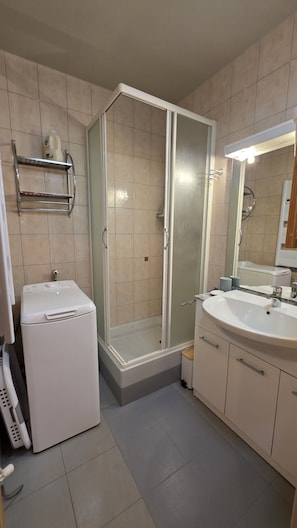 Ein Badezimmer mit Dusche, Waschbecken, Spiegel und Waschmaschine.