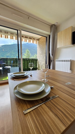 Ein Esstisch mit Tellern, Besteck und Weingläsern, vor einer Aussicht auf eine malerische Berglandschaft durch große Fenster.