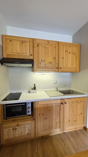Eine kompakte Küche mit Holzausstattung, Backofen, Kochfeld und Spüle.