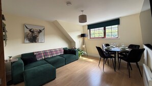 Una stanza in stile loft con un divano verde, un tavolo da pranzo con sedie, una grande finestra con vista e una ventola a soffitto.