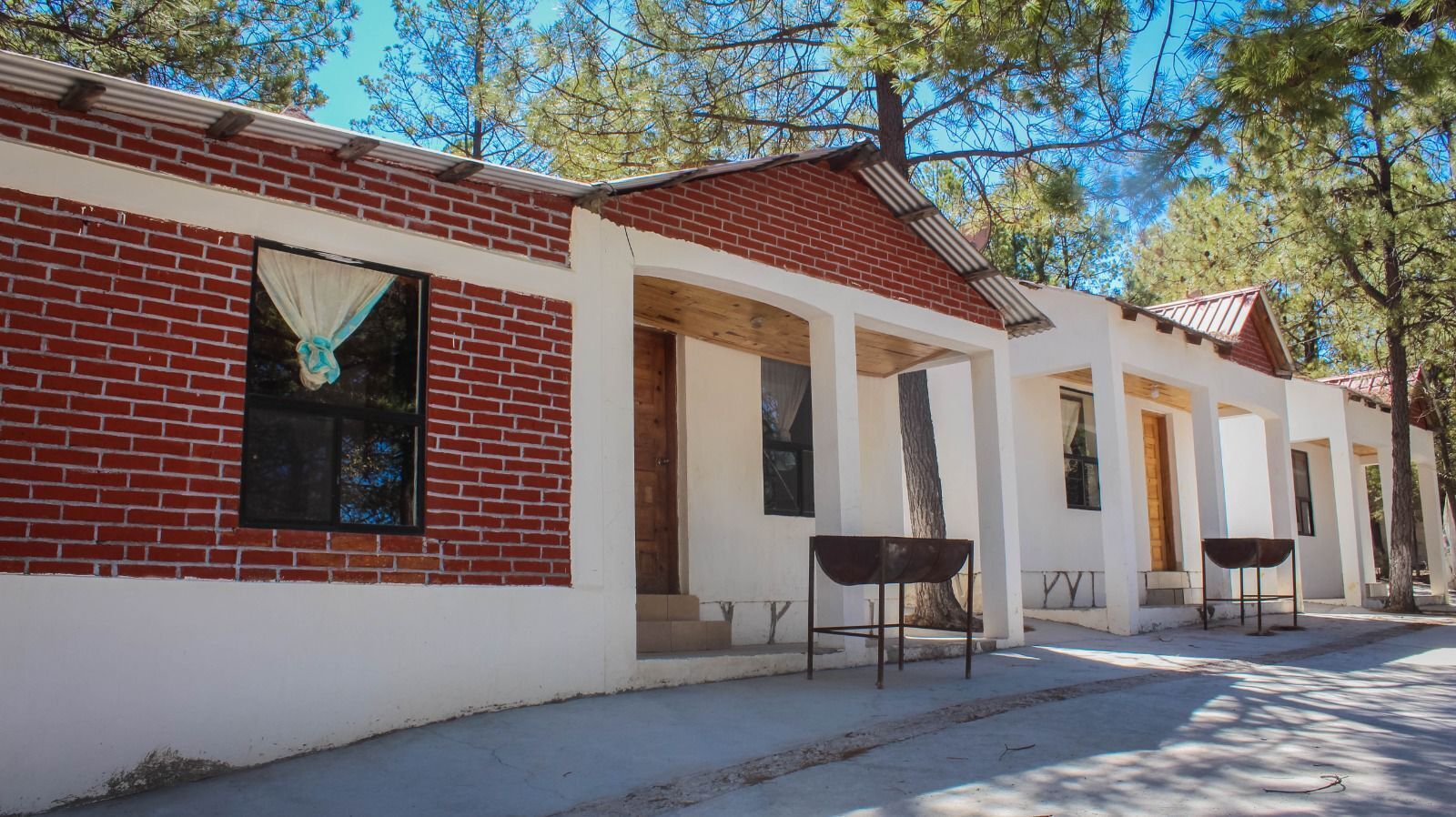 A row of single-story buildings with brick facades and white walls, each with a door and a window.