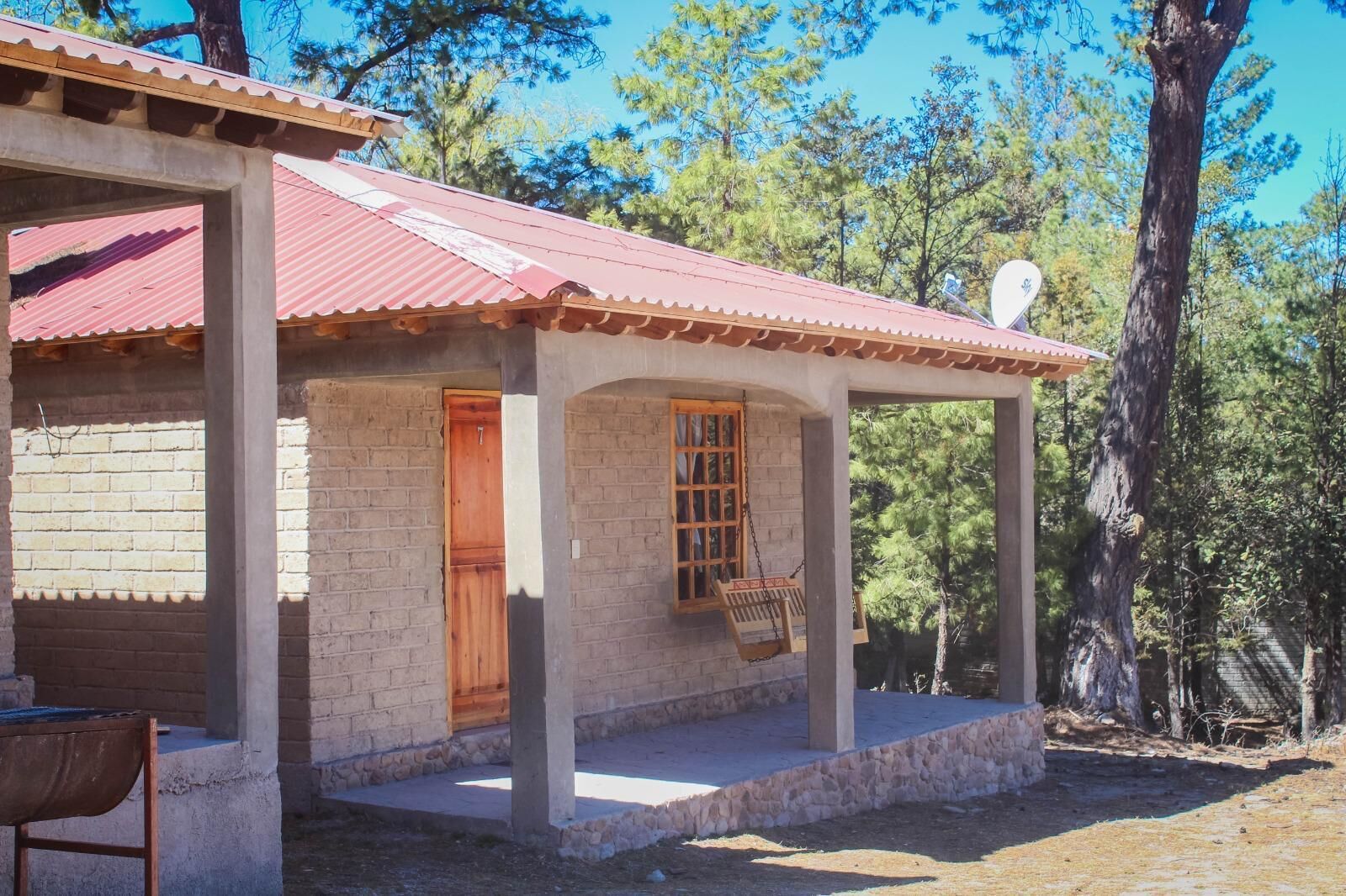 A small house with a red roof, a wooden door, and a porch with a swing.