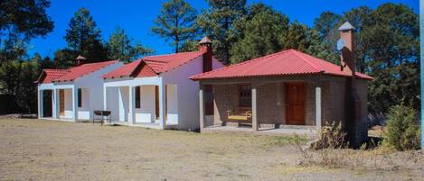 A row of single-story buildings with red roofs, a gravel driveway, and a clear blue sky.