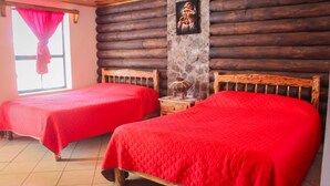 A room with two wooden beds, a stone wall, and a window with red curtains.