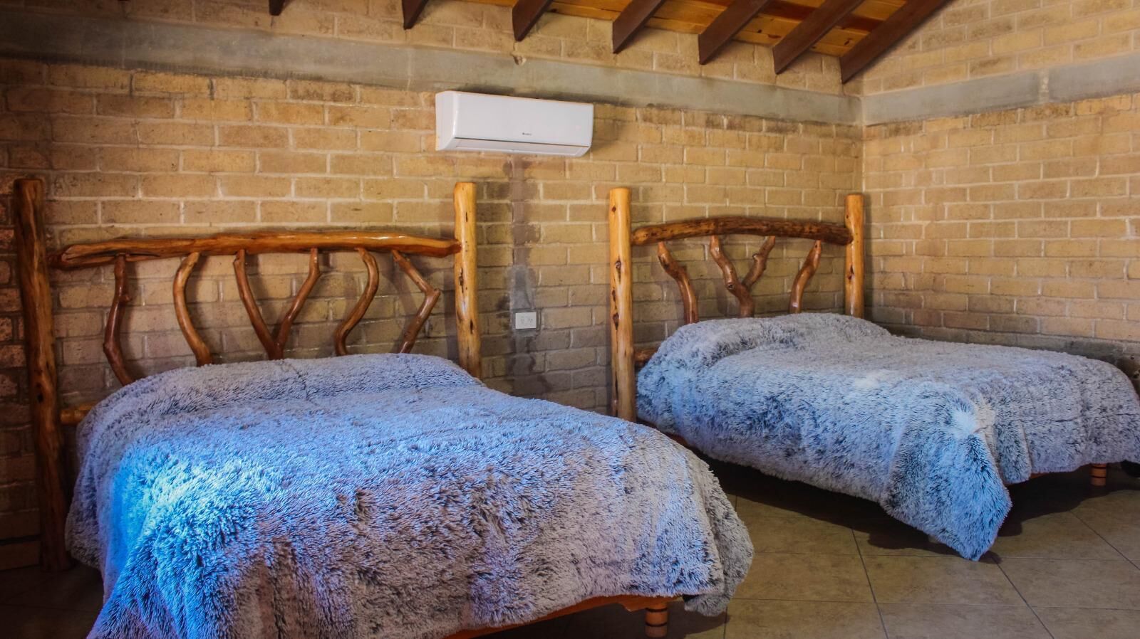Dos camas de madera con una pared de ladrillo y un equipo de aire acondicionado encima.