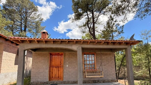 A rustic stone building with a wooden door and window, a porch with a swing, and a chimney.