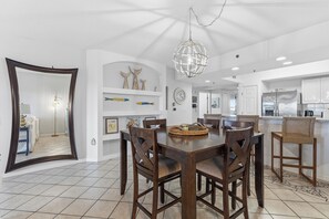 A dining area with a wooden table and chairs, a large mirror, and a hanging light fixture. - 🌴Family Friendly Beach Condo | 5 Min Walk to Beach | Oceanwalk 4-404😍🐟🦈 (New Smyrna Beach)