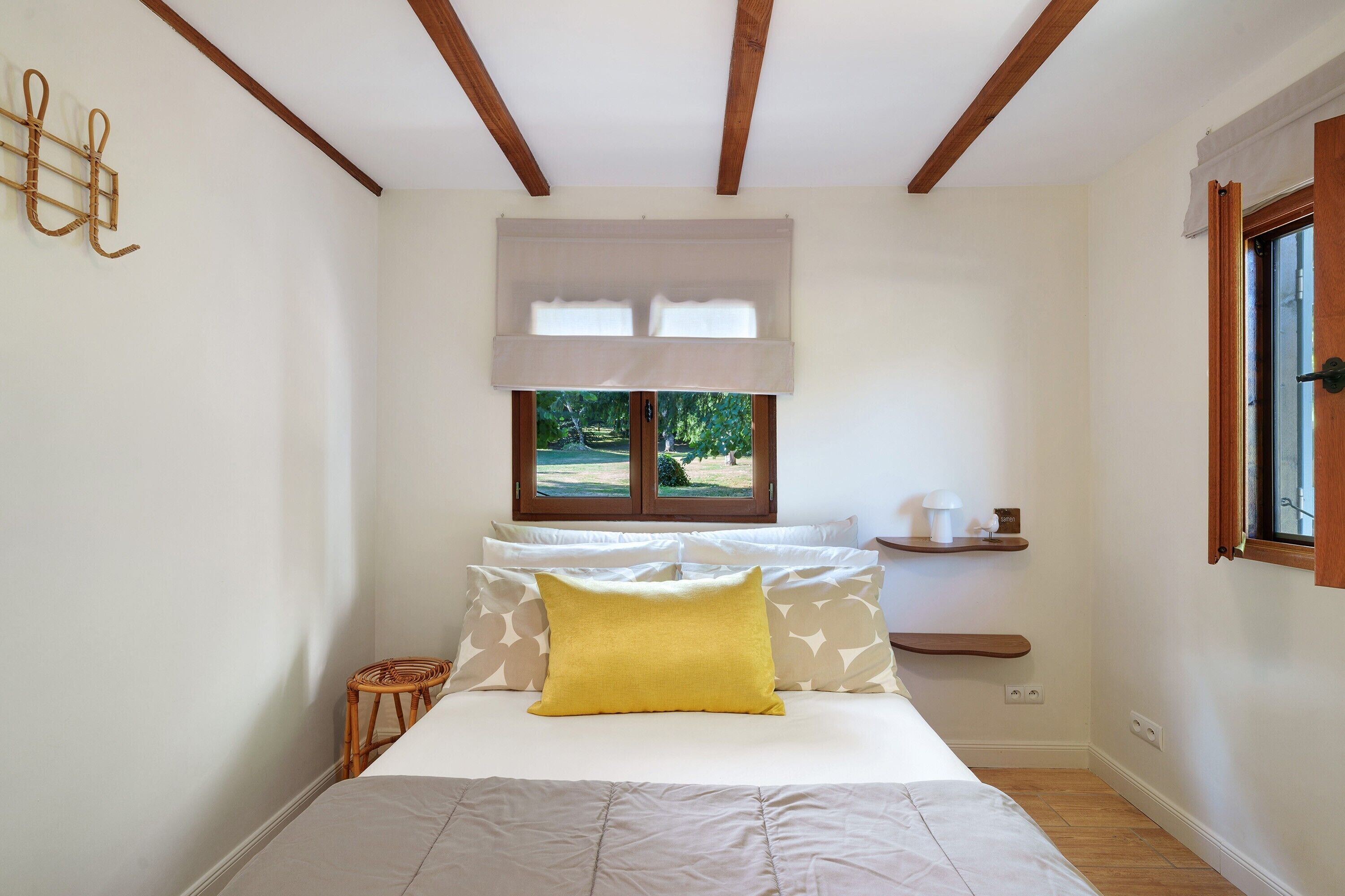 Une chambre à coucher avec un lit, une fenêtre donnant sur un beau paysage, une table de chevet et une étagère fixée au mur.