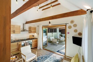 A modern kitchen with wooden beams, a stove, and a dining area with a TV and seating.