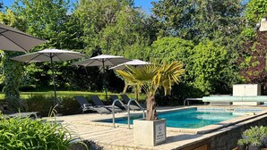 En pool med trin ned til den, omgivet af grøn vegetation og parasoller.