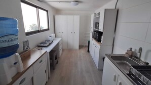 Una cocina estrecha con armarios blancos, una encimera con dispensador de agua, microondas y fregadero.