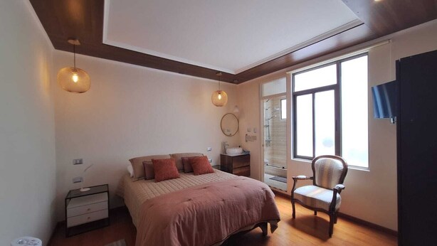 Un dormitorio con cama, mesita de noche, silla y un ventanal grande.