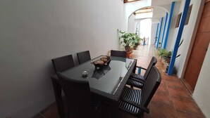Un comedor con una mesa y sillas, una planta en maceta y vistas a un pasillo con pilares azules.