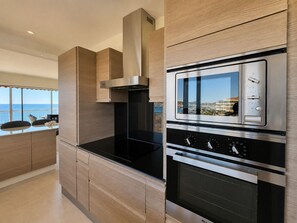 A modern kitchen with a built-in oven and microwave, a stainless steel range hood, and a view of the sea. - Apt 4 guests in Fréjus plage - sea view (Fréjus)