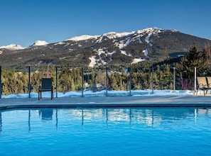 Ein Schwimmbad mit Liegestühlen, umgeben von Bäumen und einem Berg im Hintergrund.