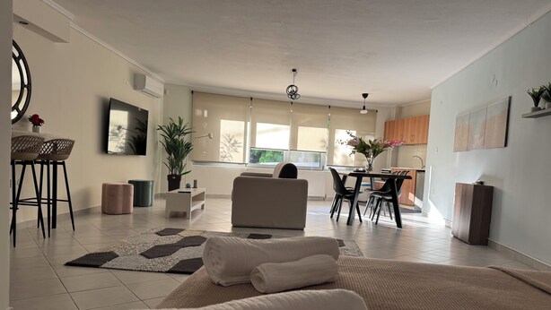 Una sala moderna con sofá, comedor con mesa y sillas, cocina al fondo y un amplio ventanal que proporciona luz natural.