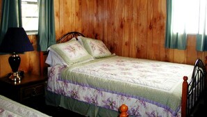 Een kamer met houten lambrisering, een bed, een nachtkastje en een lamp.