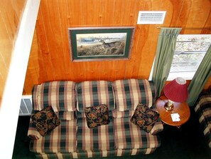Una habitación acogedora con un sofá de cuadros, un cuadro en la pared y una mesita de noche con una lámpara.