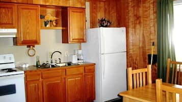 A kitchen with wooden cabinets, a white refrigerator, a stove, a sink, and a dining table with chairs.