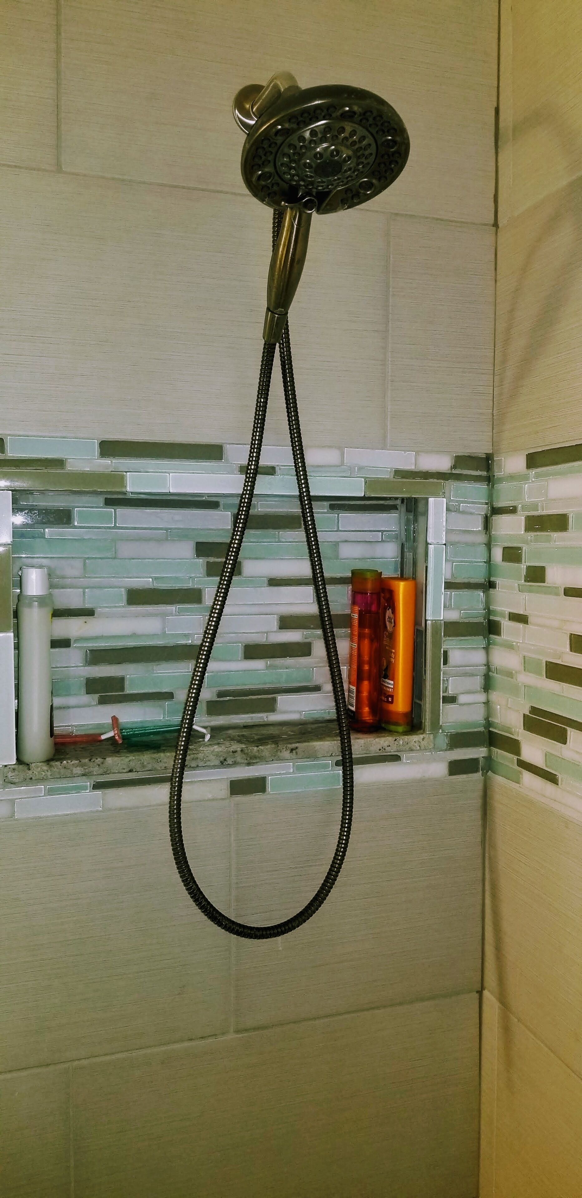 Una ducha con cabezal de ducha de mano, pared con azulejos y un estante con artículos de aseo.
