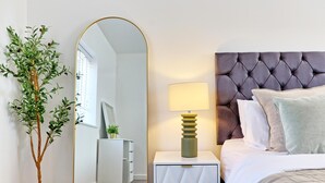 Ein Schlafzimmer mit Bett, Nachttischlampe, Spiegel und einer Topfpflanze.