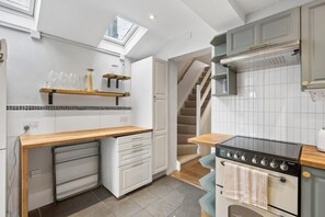 A kitchen with a built-in oven, a wooden countertop, a small refrigerator, and a staircase leading to another level.