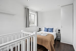 Ein Schlafzimmer mit einem weißen Babybett, einem Bett mit blauen Kissen, einem Fenster mit Vorhängen und einem Kleiderschrank.