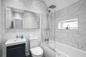 Een badkamer met toilet, wastafel, spiegel, douche en een raam.