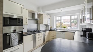 Una cucina moderna con mobili bianchi, un piano di lavoro nero, elettrodomestici in acciaio inossidabile e una finestra con vista all'esterno.