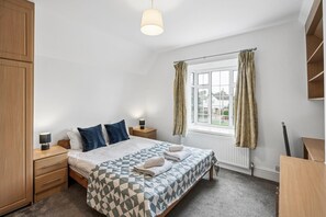 Een slaapkamer met een bed, nachtkastjes, een lamp, een raam met gordijnen en een radiator.