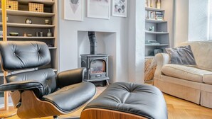 Una sala de estar moderna con un sofá, dos sillones de cuero, un reposapiés de madera, una chimenea y estantes con objetos decorativos.