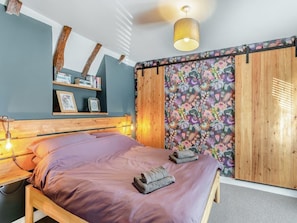 A bedroom with a bed, bedside lamps, a wooden headboard, a wall-mounted shelf with books, and a floral wallpaper. - Beautiful Country 3 Bed Escape, Warwickshire - Pass the Keys (Ufton)