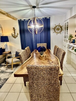 Ein Essbereich mit Holztisch, gewebten Stühlen, einer Kristallleuchter und maritimer Dekoration.