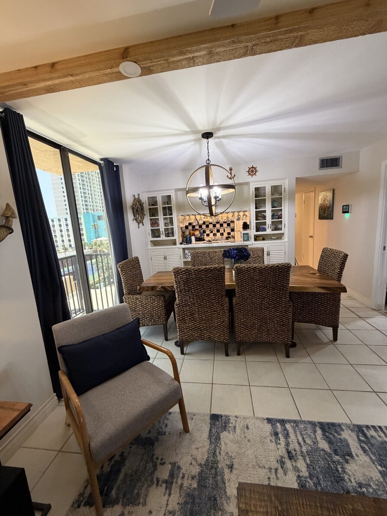A dining area with a chandelier, a dining table with chairs, a view through a window, and a door with a painting.