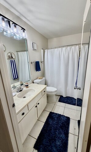 Ein Badezimmer mit einem weißen Waschbecken, einer Toilette, einem Duschvorhang und einem blauen Teppich.