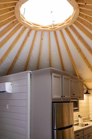A circular skylight in a wooden ceiling, a stainless steel refrigerator, and a kitchen with white cabinets.