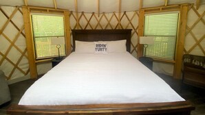 A bed in a tent with a wooden headboard, two bedside tables, and a pillow with text. - Fully-Equipped Yurt Rental for Memorable Family Vacations in Livingston, Texas (Livingston)